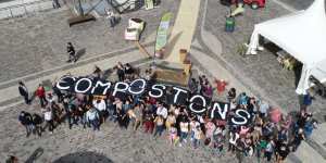 Une vue aérienne d'un groupe de personnes, tenant des lettres qui forment le mot "Compostons"