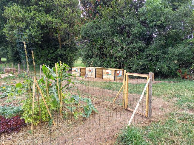 3 bacs de compostages en bois derrière une parcelle des jardins partagés