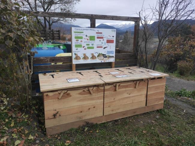 Emplacement de la plateforme sur le point de collecte en dessous de l'église. Module en bois avec panneau explicatif.